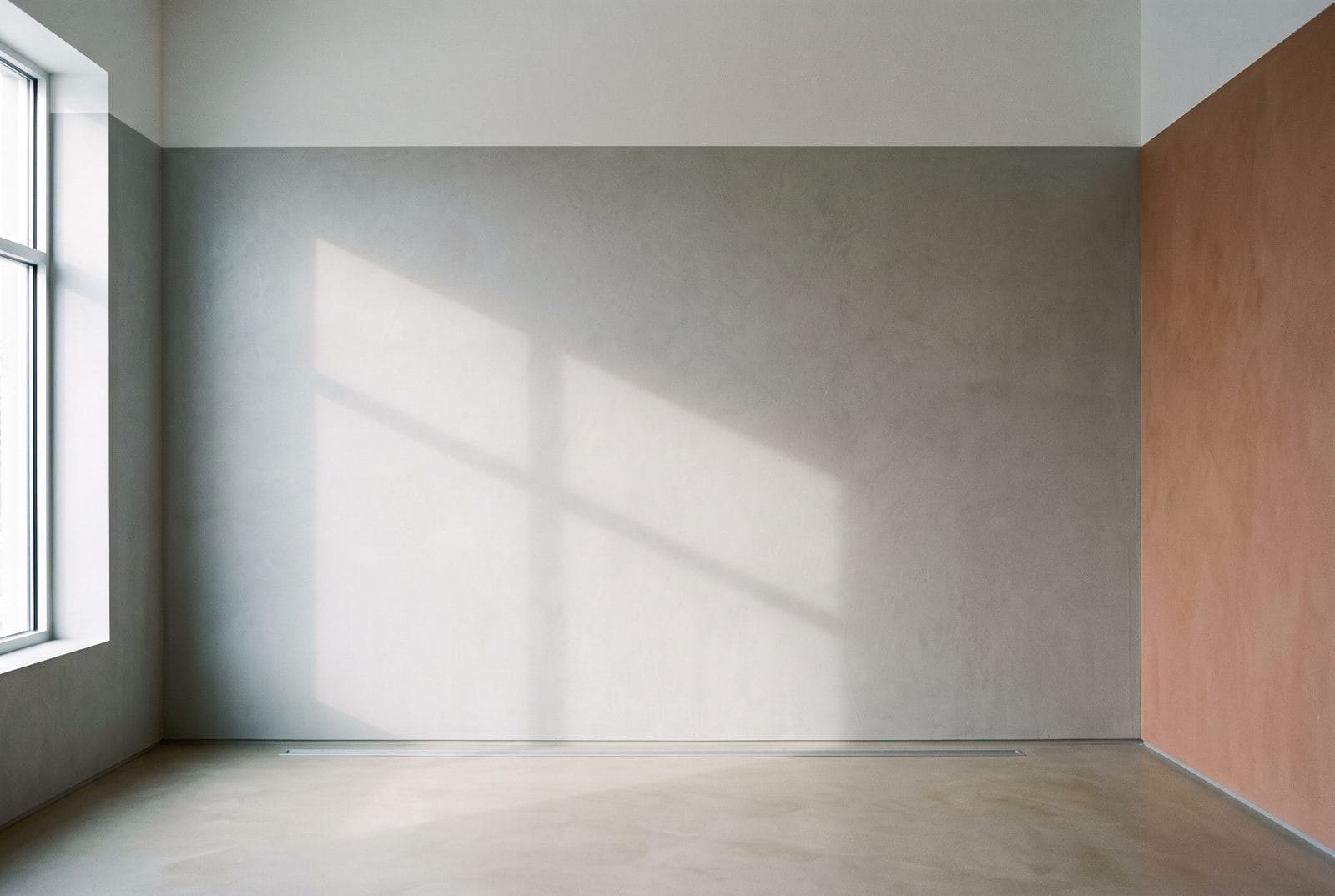 A band of daylight and the soft shadow of a window frame falling across a plain pale wall.